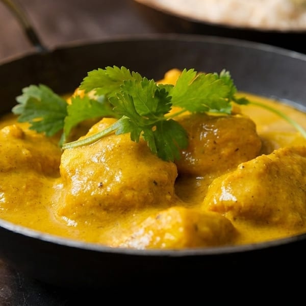 Chicken curry in a black bowl, garnished with fresh cilantro, with rice in the background.