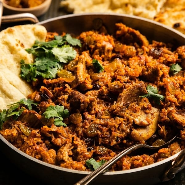 Close-up of a pan filled with chicken biryani, garnished with cilantro and served with naan bread.