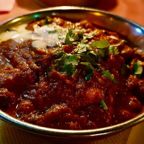Rich red curry with cream and fresh cilantro in a decorative metal bowl.